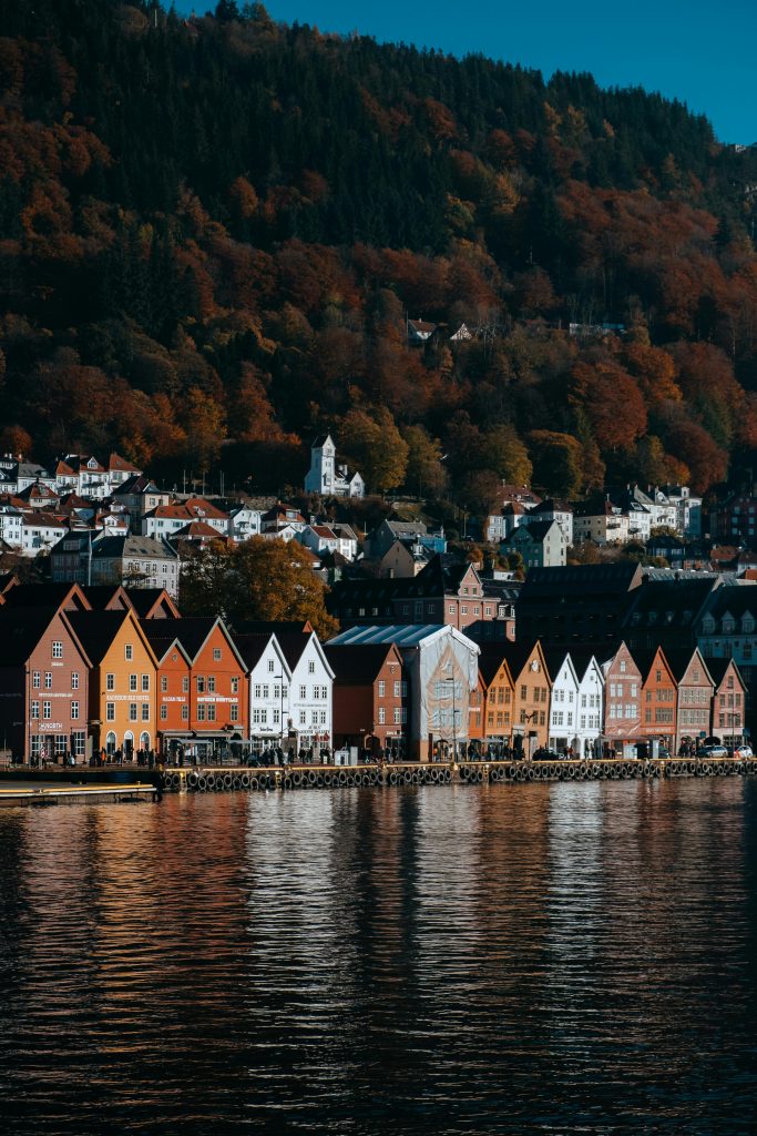 Colorful houses reflect on the fjord in Bergen, Norway, showcasing autumn's beauty.